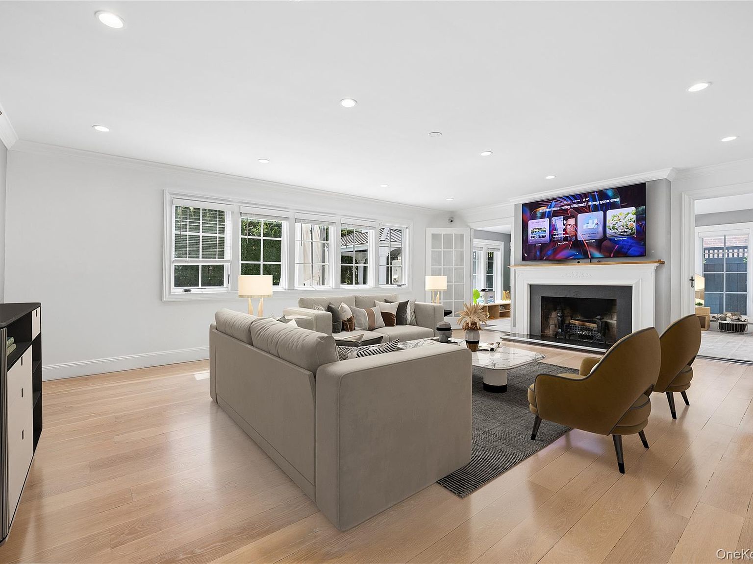 Open-plan family room at 216 Beverly Road. Original-detail mantel with a working fireplace, recessed lighting, and the wall of divided-light windows that frames the rear of the house.