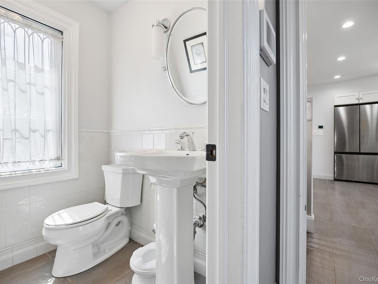 The powder room and a glimpse down the hall toward the kitchen. Period subway-tile wainscot, pedestal sink, and the home's restored white millwork.